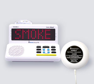 A white HomeAware II main unit with a red LED display reading 'SMOKE' and a matching white bed shaker, shown on a light gray background.