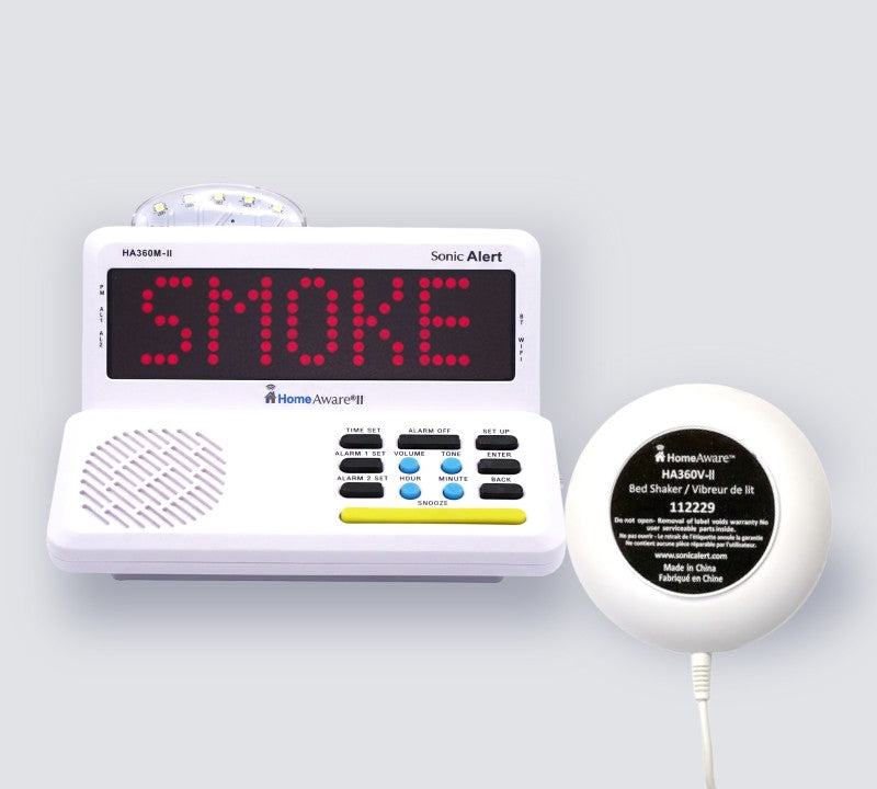 A white HomeAware II main unit with a red LED display reading 'SMOKE' and a matching white bed shaker, shown on a light gray background.